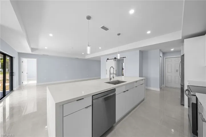 Kitchen featuring a barn door, white cabinetry, appliances with stainless steel finishes, light stone counters, and open floor plan