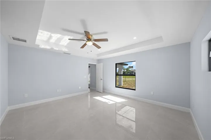 Spare room with a tray ceiling, a ceiling fan, and light tile patterned floors