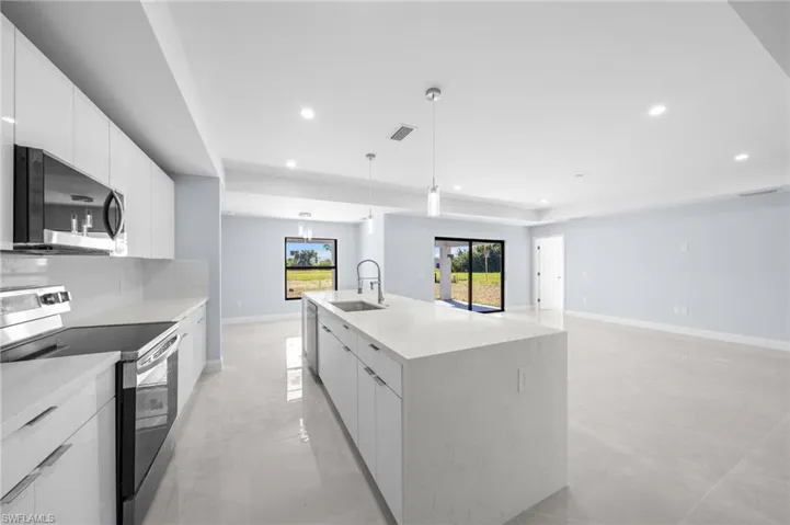 Kitchen with appliances with stainless steel finishes, white cabinets, a spacious island, modern cabinets, and light stone countertops
