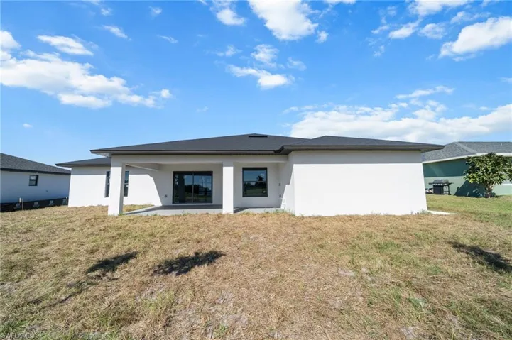 Rear view of house featuring stucco siding, a lawn, and a patio area