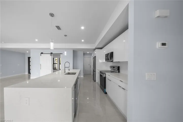 Kitchen with a barn door, white cabinetry, stainless steel appliances, a spacious island, and pendant lighting