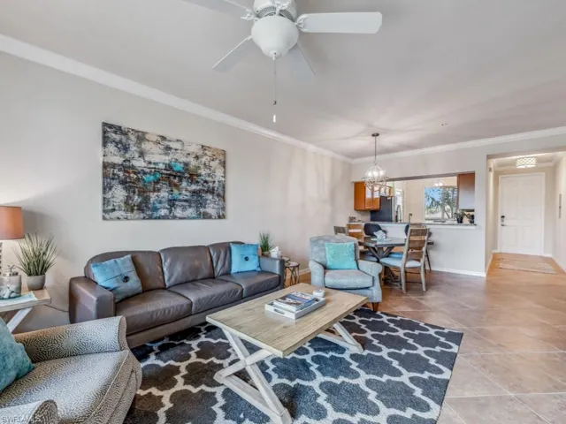 Tiled living room featuring ceiling fan with notable chandelier and ornamental molding