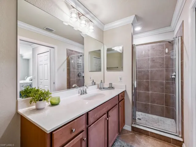 Bathroom with an enclosed shower, vanity, ornamental molding, and tile patterned flooring