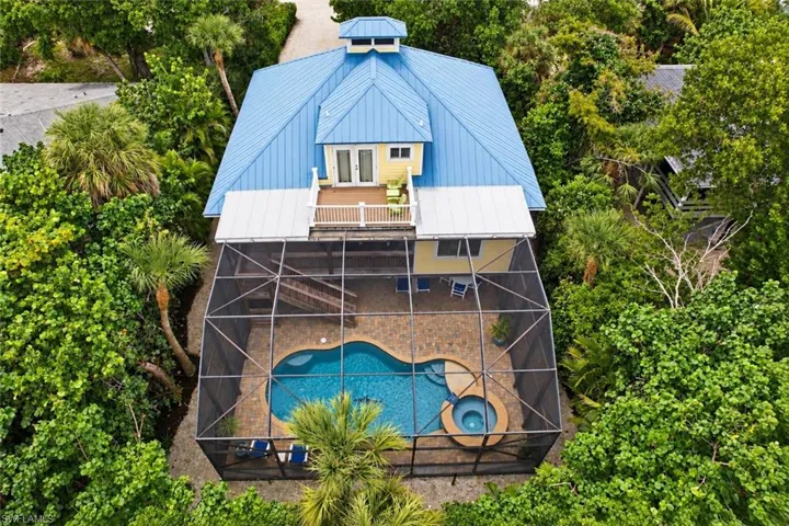 Property featuring a bright blue metal roof and dormer, a screened-in pool enclosure, a free-form swimming pool, and an integrated spa