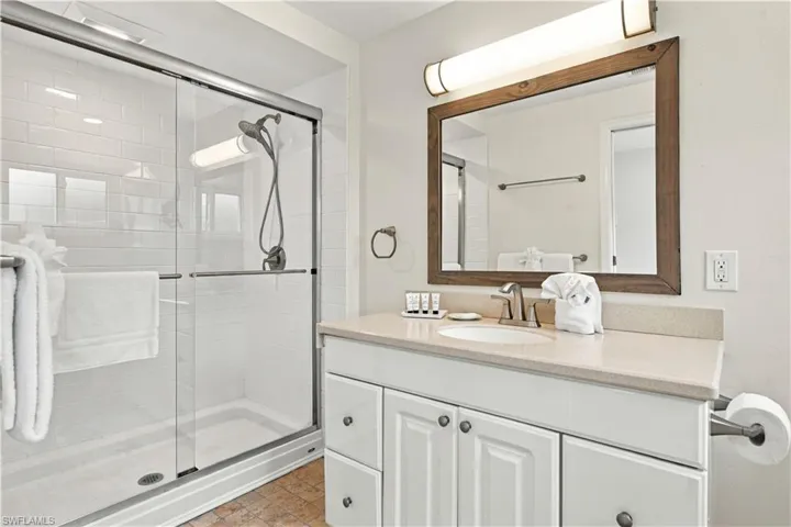 Glass-enclosed shower with subway tile surround, single vanity with light-toned countertop, and framed mirror with integrated lighting