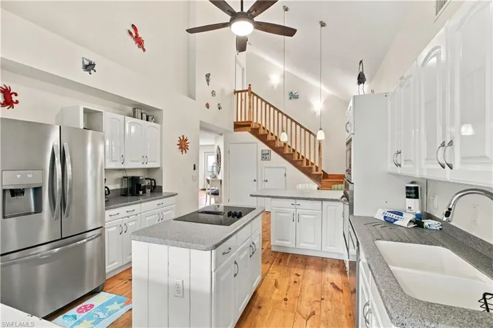Kitchen island with integrated cooktop, white cabinetry, stainless steel refrigerator, and wood-finish flooring