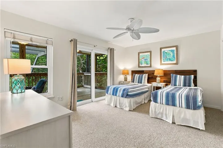 Carpeted flooring, white walls, wood panel headboards, ceiling fan, and sliding glass door to exterior decking