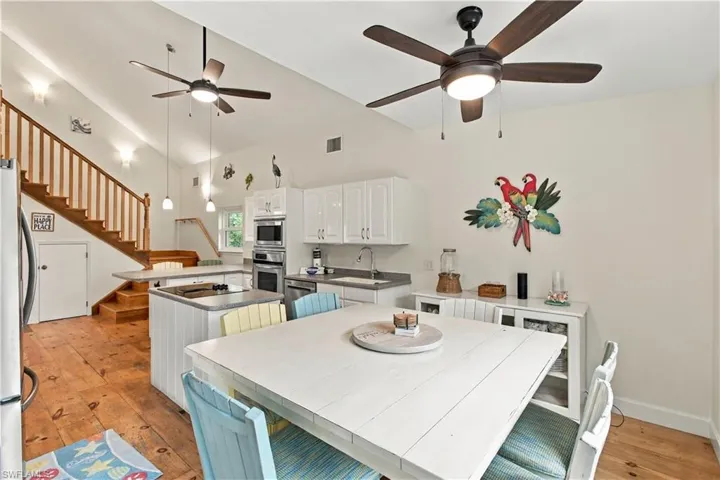 Vaulted ceilings with ceiling fans, wood-finish flooring, white cabinetry, stainless steel appliances, and a built-in kitchen island