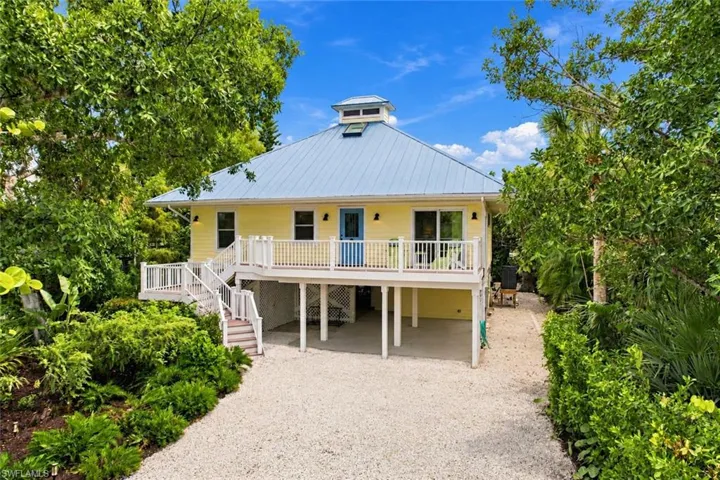 Elevated residence featuring a light yellow exterior, blue metal roof, and a cupola
