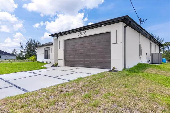 View of front of property featuring stucco siding, central air condition unit, a front lawn, driveway, and a garage