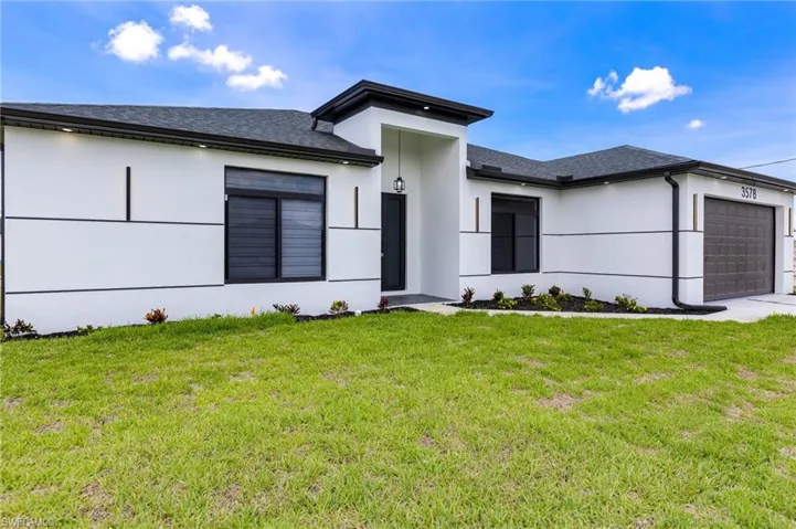 View of front facade with an attached garage, stucco siding, a front lawn, roof with shingles, and driveway