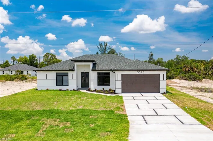 View of front of home featuring stucco siding, a garage, roof with shingles, a front yard, and driveway