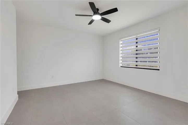 Tiled empty room with a ceiling fan and baseboards