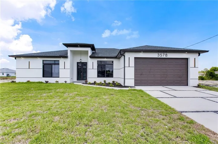 View of front facade featuring stucco siding, driveway, an attached garage, a front lawn, and a shingled roof