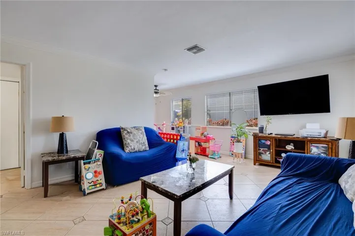 Living area with ornamental molding, light tile patterned flooring, and ceiling fan