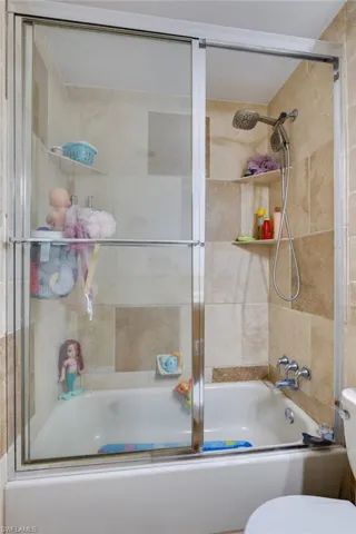 Bathroom featuring combined bath / shower with glass door and toilet