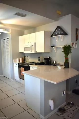 Kitchen featuring light stone countertops, kitchen peninsula, light tile flooring, range with electric stovetop, and white cabinetry