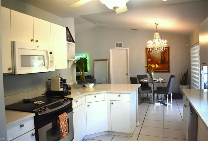 Kitchen with white cabinetry, lofted ceiling, ceiling fan with notable chandelier, decorative light fixtures, and electric stove