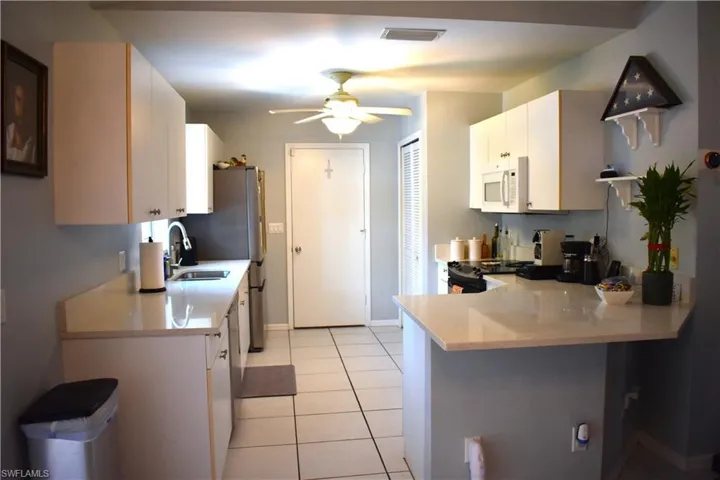 Kitchen with white cabinetry, kitchen peninsula, sink, ceiling fan, and light tile floors