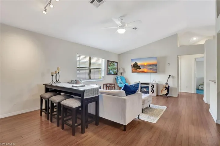 Living area featuring light wood-style flooring, ceiling fan, vaulted ceiling, and a glass covered fireplace
