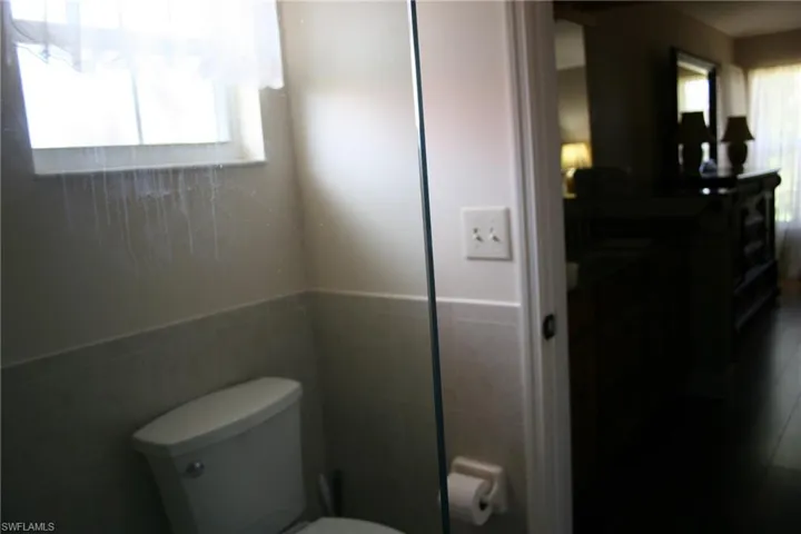 Bathroom featuring a wainscoted wall, a healthy amount of sunlight, toilet, and tile walls