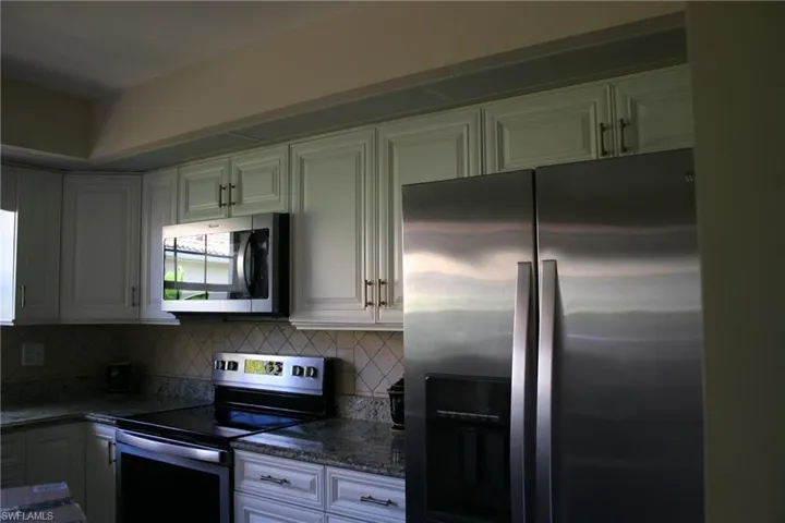 Kitchen featuring appliances with stainless steel finishes, backsplash, dark stone countertops, and white cabinetry