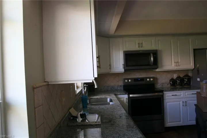 Kitchen featuring a sink, stone counters, backsplash, and stainless steel appliances