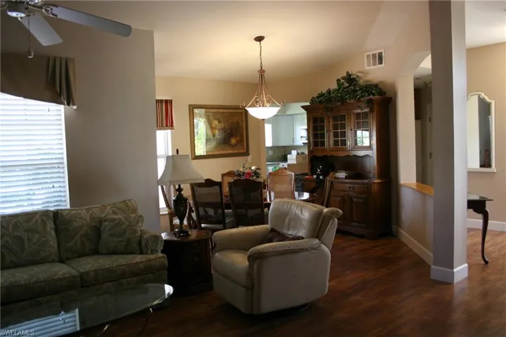 Living room with arched walkways, a ceiling fan, visible vents, and dark wood-style floors