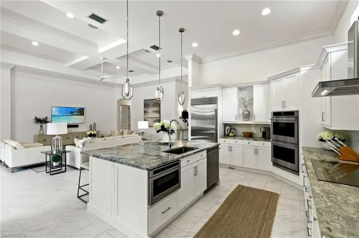 Kitchen featuring open floor plan, a kitchen bar, dark stone countertops, hanging light fixtures, and coffered ceiling