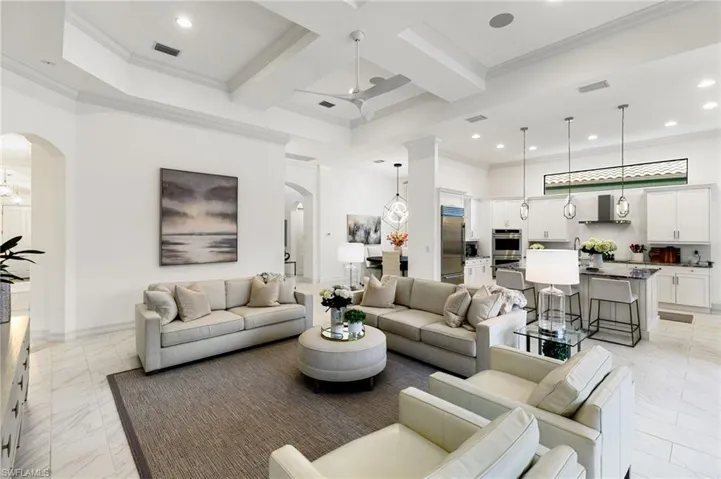 Living room featuring arched walkways, crown molding, coffered ceiling, light marble finish floors, and recessed lighting