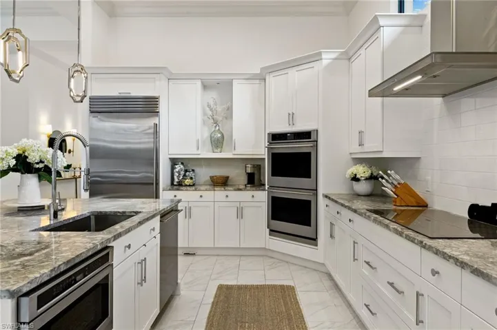 Kitchen with light stone countertops, white cabinets, stainless steel appliances, decorative light fixtures, and ornamental molding