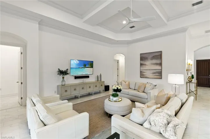 Living area with arched walkways, light marble finish floors, crown molding, coffered ceiling, and a ceiling fan