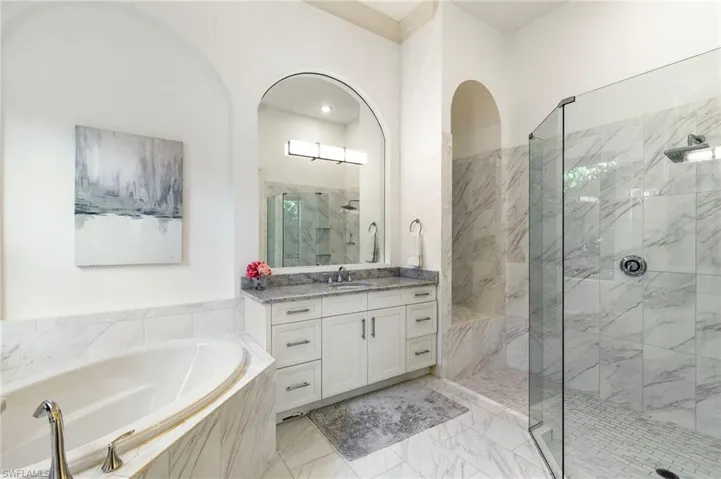 Bathroom featuring a marble finish shower, vanity, a bath, and light marble finish floors