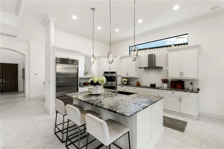 Kitchen featuring white cabinets, dark stone countertops, arched walkways, a kitchen island with sink, and a breakfast bar