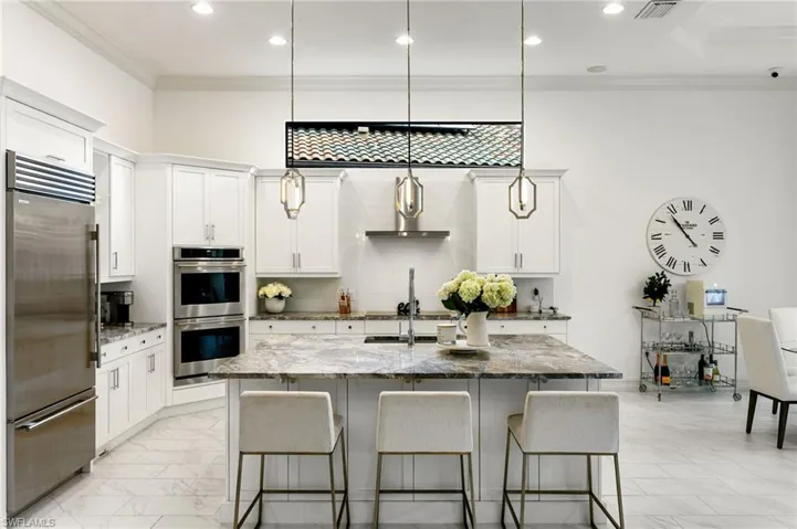 Kitchen with dark stone countertops, stainless steel appliances, ornamental molding, a kitchen bar, and a kitchen island with sink