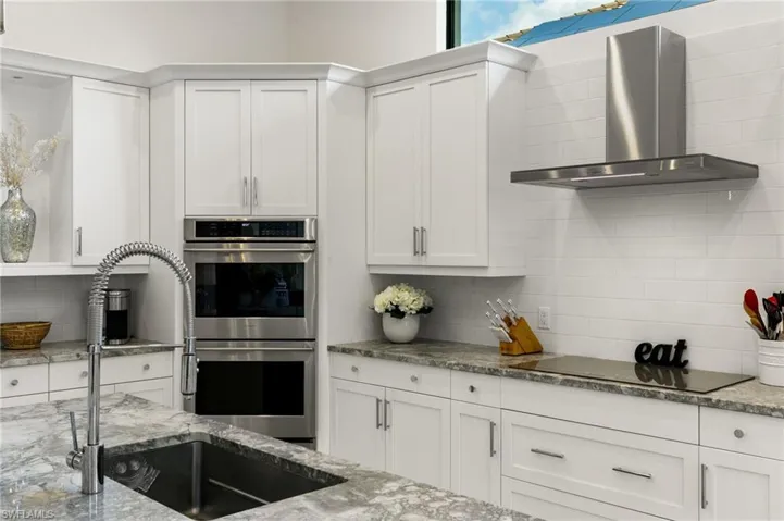 Kitchen with white cabinetry, stainless steel double oven, tasteful backsplash, and light stone counters