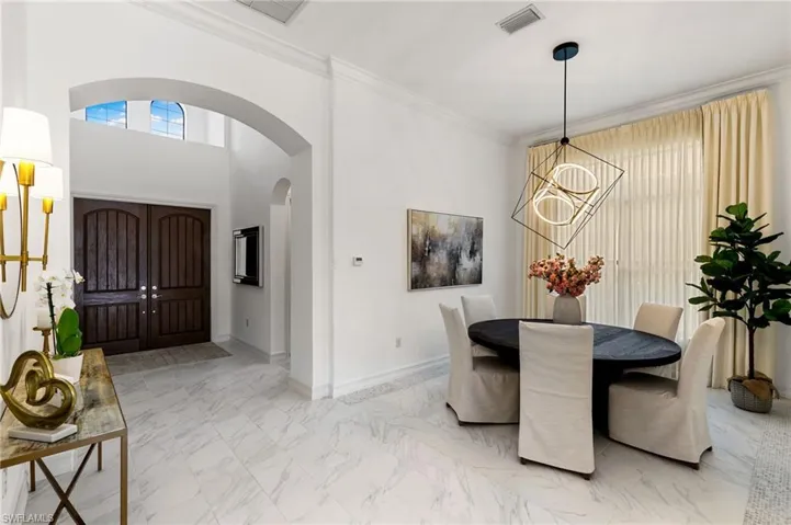 Dining space with marble look tile flooring, arched walkways, a chandelier, crown molding, and a high ceiling