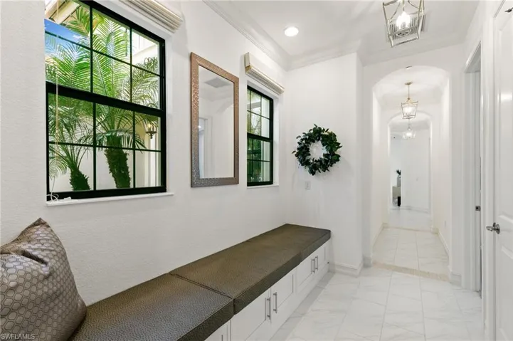 Mudroom featuring arched walkways, hanging lights, light marble finish flooring, and crown molding
