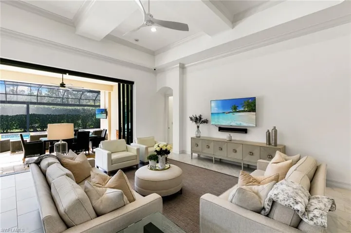 Living room featuring ceiling fan, arched walkways, ornamental molding, coffered ceiling, and a sunroom