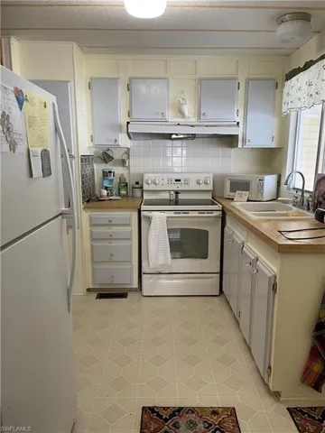 Kitchen with white cabinetry, white appliances, sink, tasteful backsplash, and light tile floors