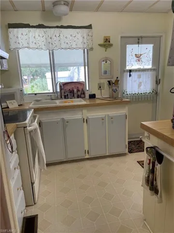 Kitchen featuring white appliances, sink, white cabinetry, and light tile floors
