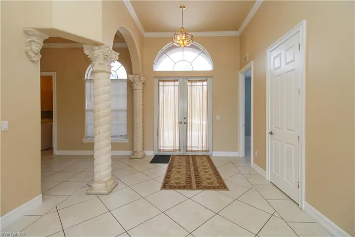 Foyer with light tile patterned floors, baseboards, french doors, decorative columns, and crown molding