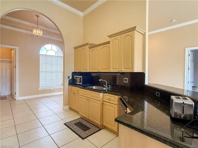 Kitchen featuring decorative light fixtures, light brown cabinets, a sink, light tile patterned flooring, and dark stone countertops