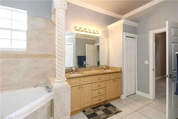 Bathroom featuring double vanity, decorative columns, ornamental molding, tile patterned flooring, and a sink