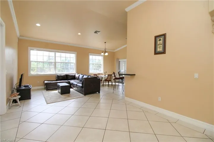 Living area with light tile patterned floors, recessed lighting, visible vents, baseboards, and ornamental molding