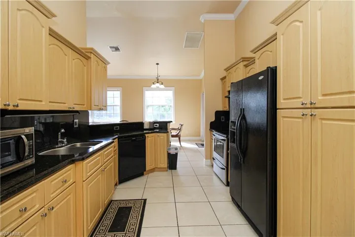 Kitchen with ornamental molding, black appliances, light brown cabinetry, and a sink