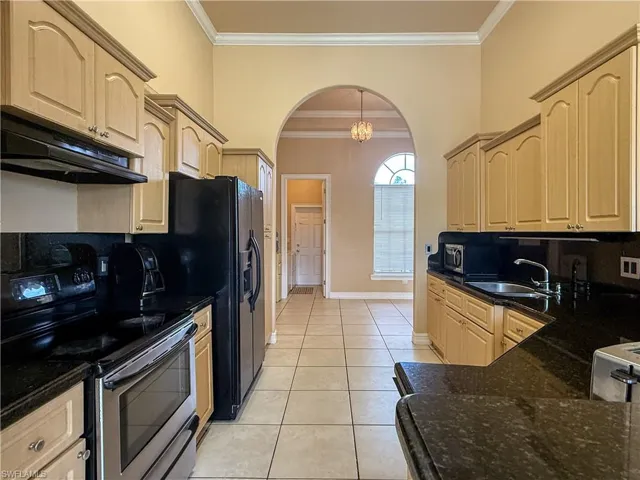Kitchen featuring arched walkways, light tile patterned floors, under cabinet range hood, electric range, and light brown cabinetry