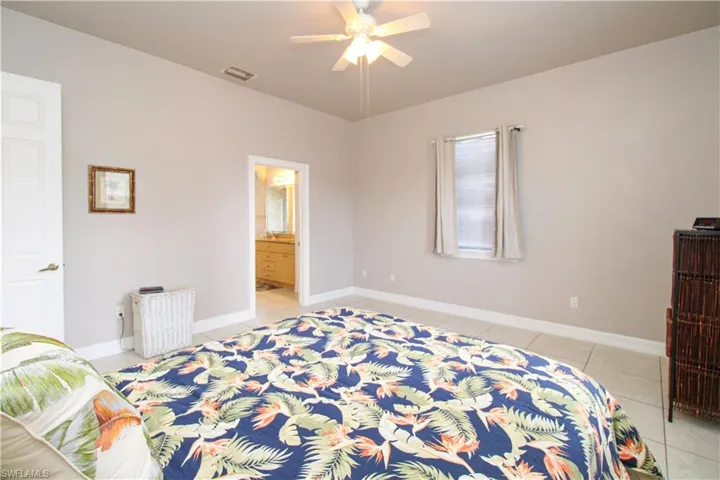 Bedroom with light tile patterned floors, a ceiling fan, visible vents, baseboards, and ensuite bath
