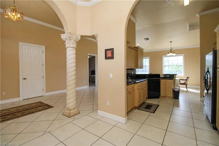 Kitchen featuring light tile patterned floors, black appliances, hanging light fixtures, and dark countertops