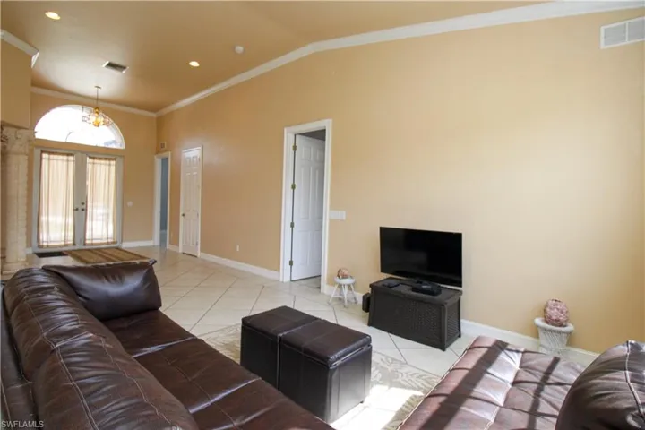 Living room featuring french doors, light tile patterned floors, lofted ceiling, visible vents, and ornamental molding